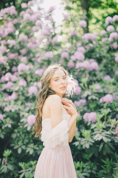 ピンクの花の近くに立っている白いドレスの女性
