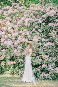 一位身穿白色连衣裙的女子站在鲜艳的粉色花朵旁，拥抱大自然