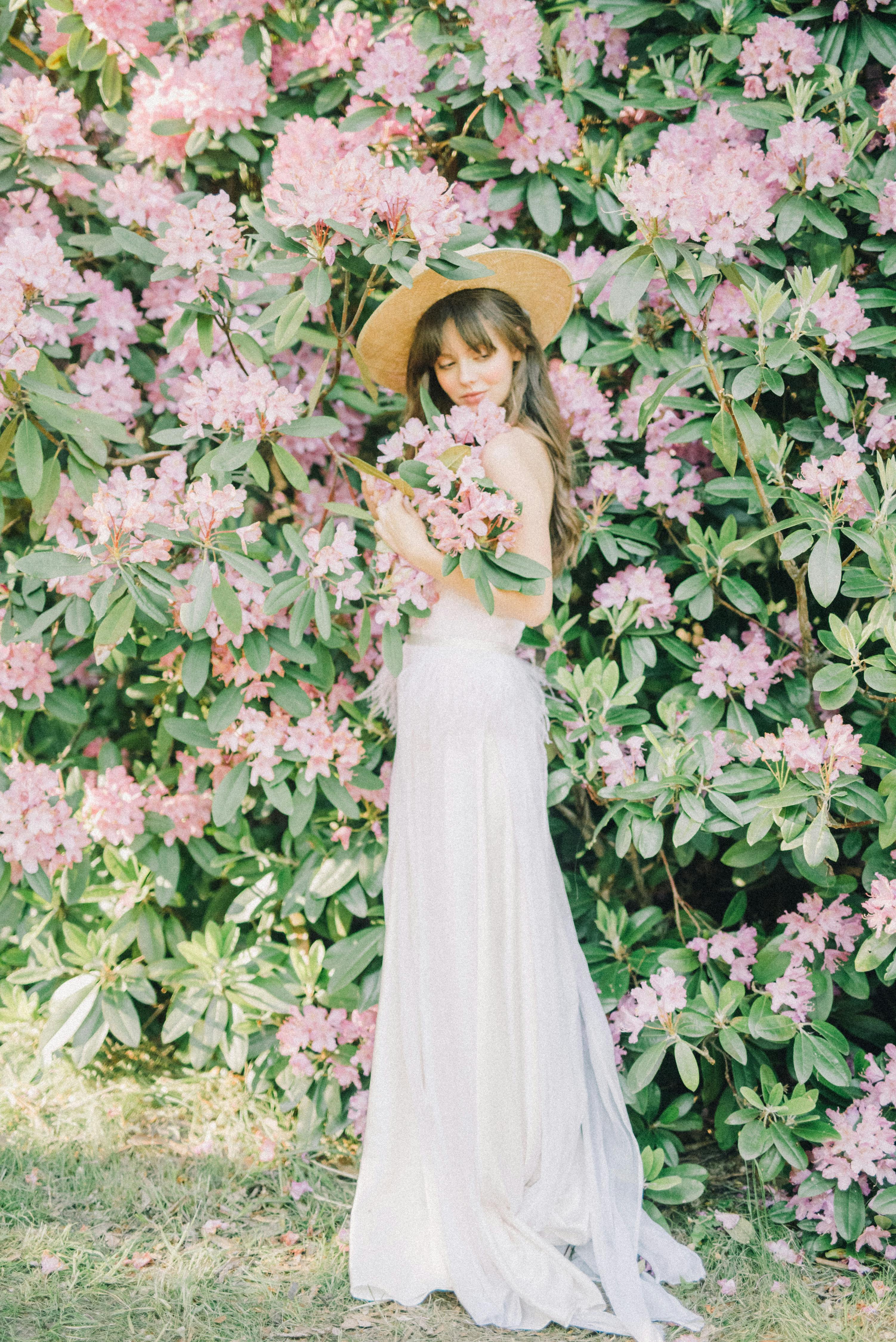 一位身穿白色连衣裙的女子，被郁郁葱葱的粉色花朵环绕，散发着优雅的气息