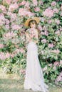 一位身穿白色连衣裙的女子，被郁郁葱葱的粉色花朵环绕，散发着优雅的气息