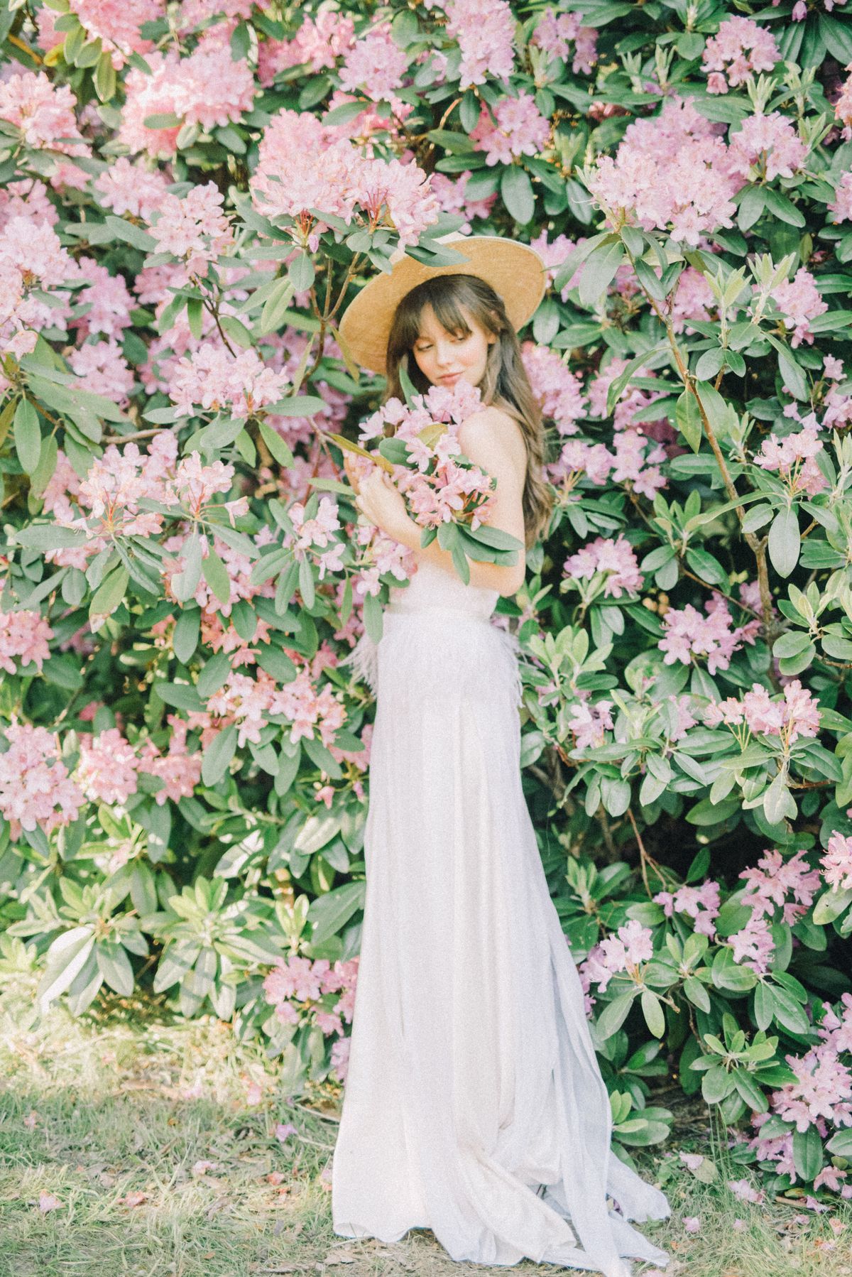 A woman in a white dress wearing a brown sun hat standing beside plants