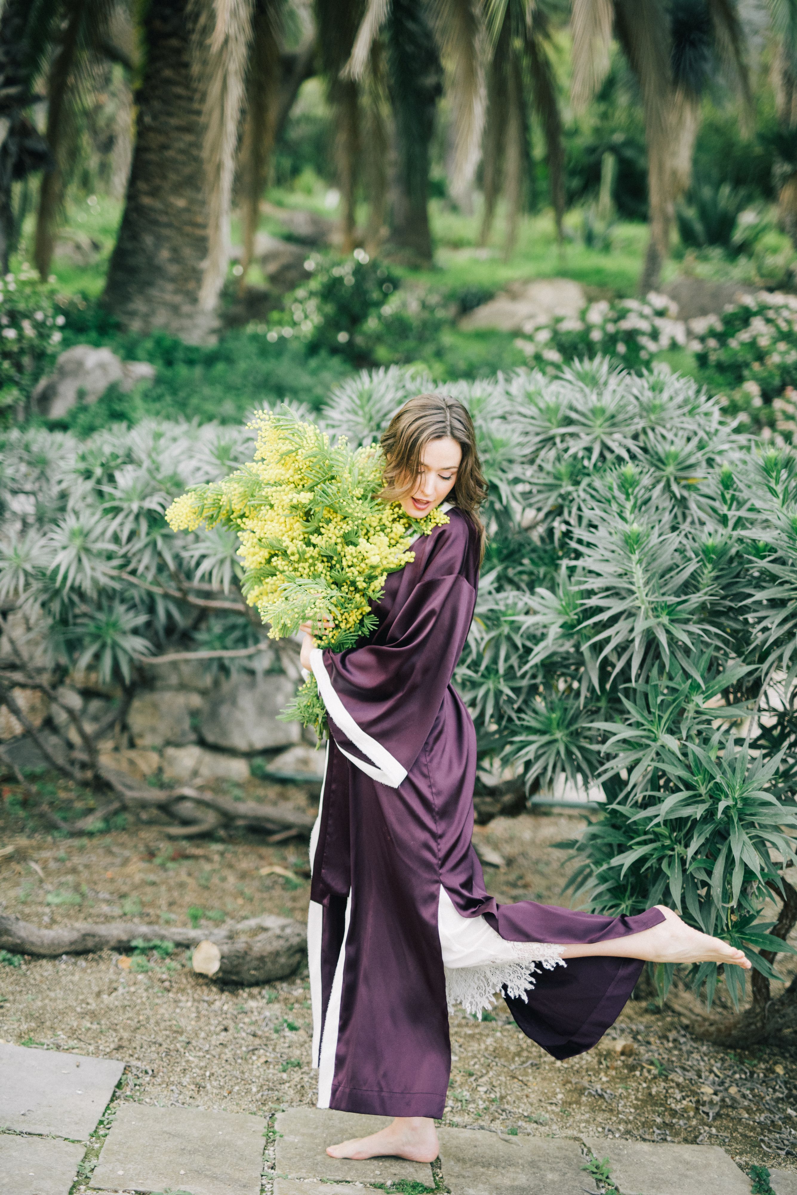 在宁静的花园中，一名身穿缎面长袍的女子优雅地捧着一束郁郁葱葱的花