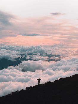 在马来西亚沙巴的拉瑙日出时分，一名旅行者拥抱云层之上的山景剪影