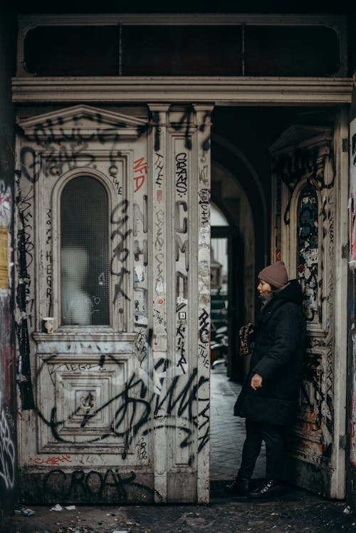 Man in Black Coat Standing in Front of White and Brown Floral Door