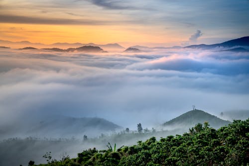Breathtaking landscape of thick clouds floating over mountains with lush green tropical foliage at sundown