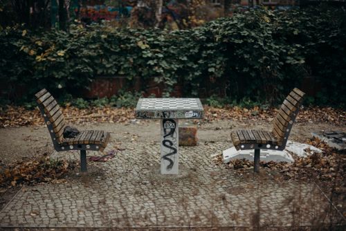 Free Two benches facing graffiti-marked table in a leafy urban park setting during fall. Stock Photo