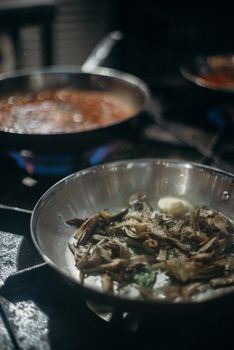 Artistic shot of cooking in stainless steel pans on a stove, focusing on gourmet food preparation.
