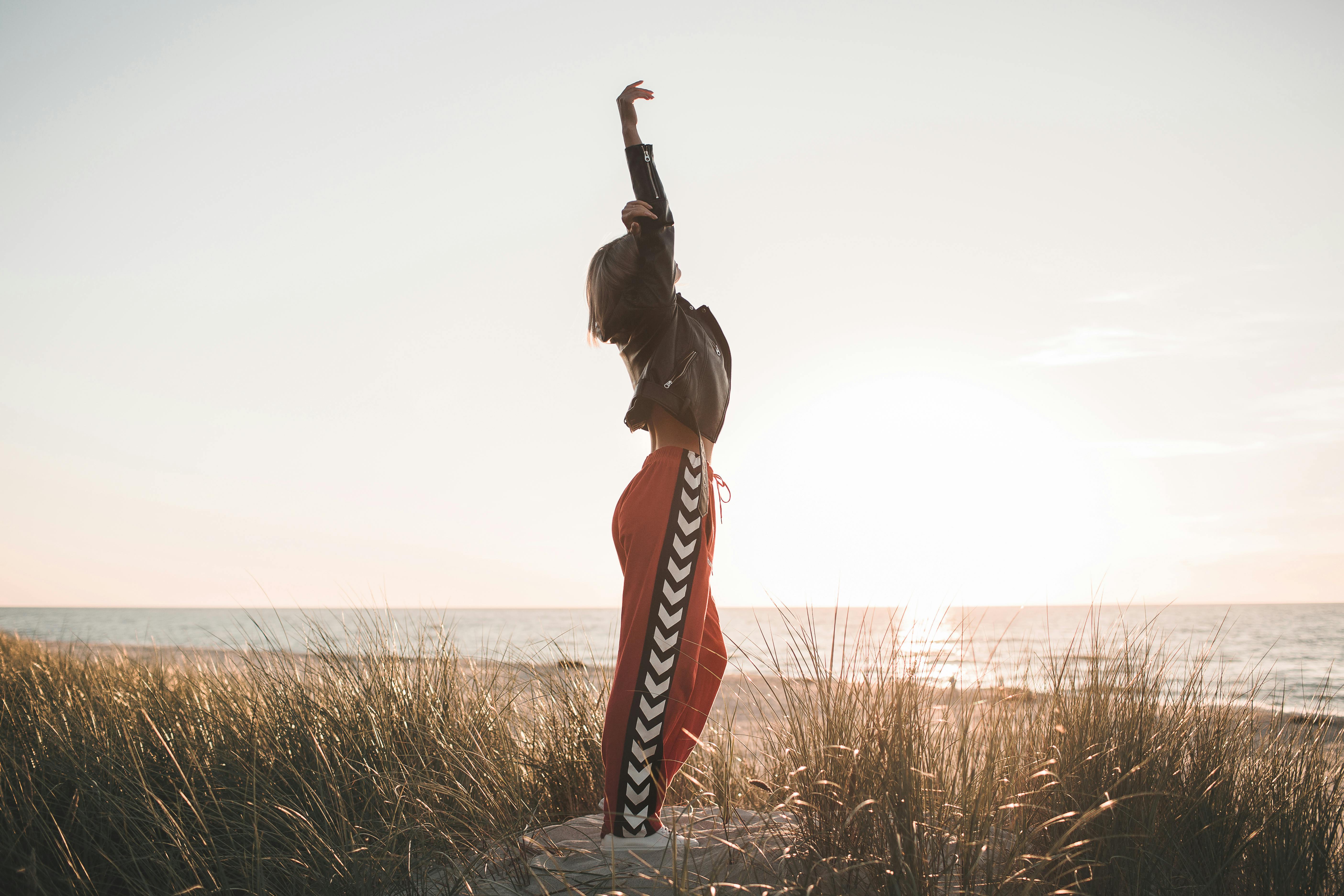 一个穿着皮夹克的女人在日落时分在海滩上伸展，体现了自由和放松