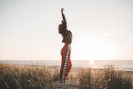 一个穿着皮夹克的女人在日落时分在海滩上伸展，体现了自由和放松