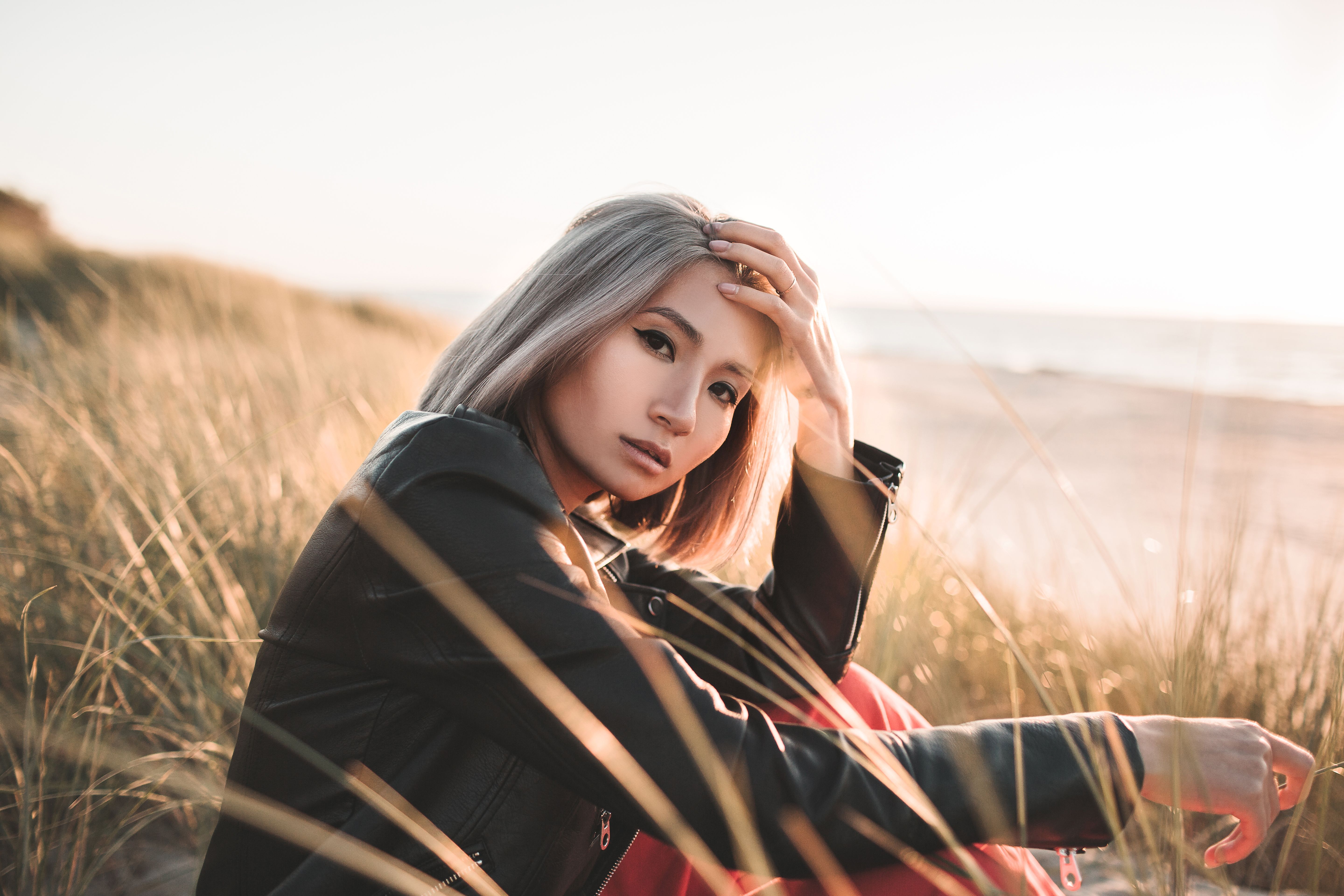 Fashionable woman posing in a leather jacket at a sunny beach shoreline.