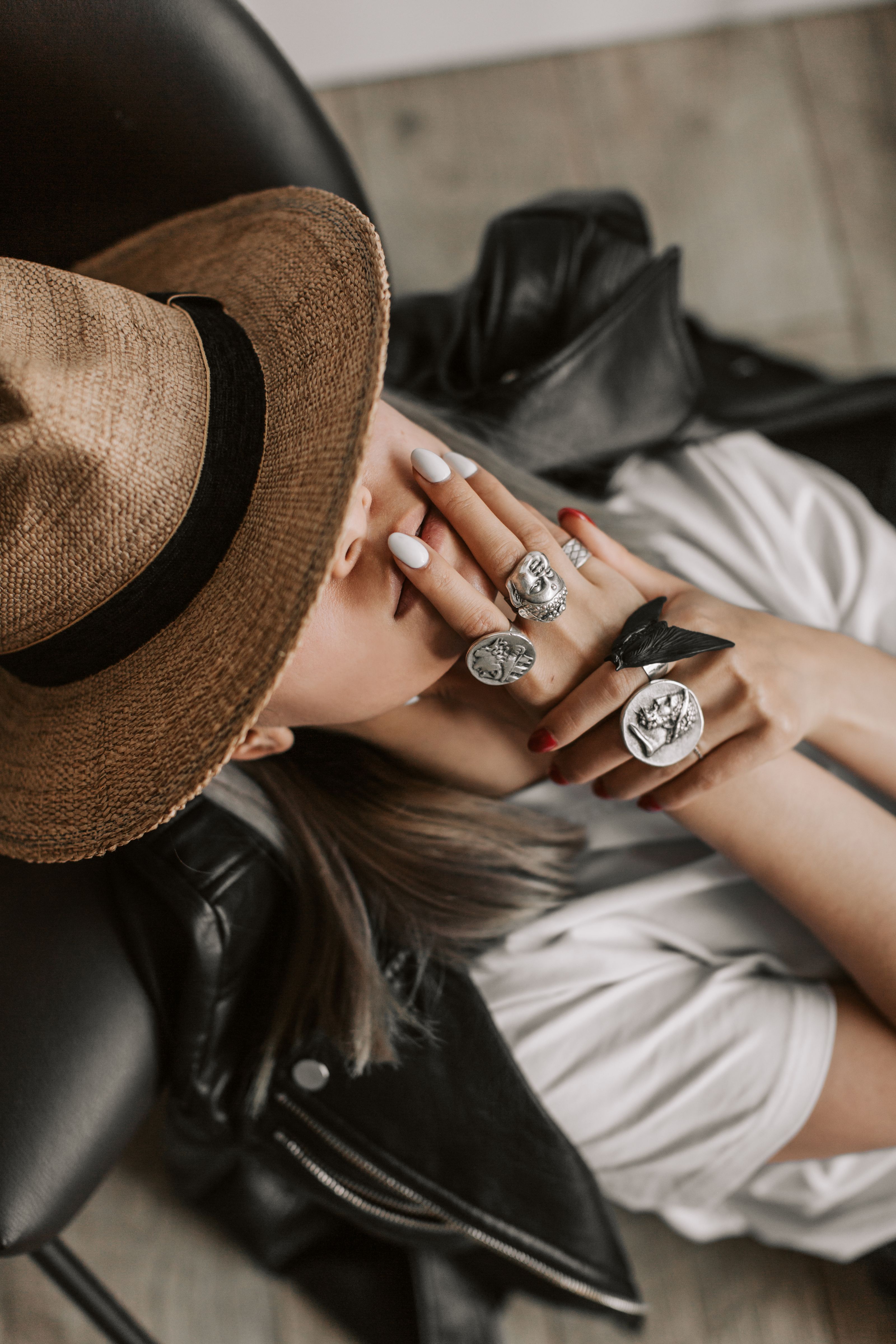 Mulher chique com chapéu de palha exibindo anéis da moda e unhas monocromáticas enquanto relaxa.