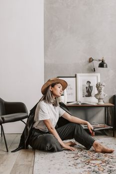 一位戴着时尚帽子的亚洲妇女，正坐在现代客厅铺着地毯的地板上