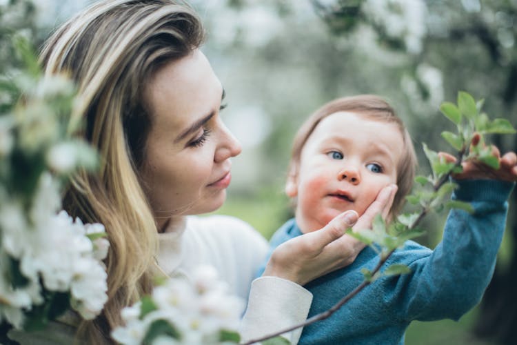 A Woman Carrying A Baby Touching The Leaves