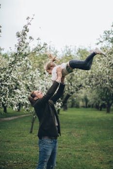 春天，一位快乐的父亲抱着女儿，在公园里盛开的树木中