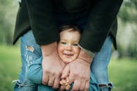 在春天的户外，一个开朗的孩子被成年人拥抱着，画面温暖而幸福