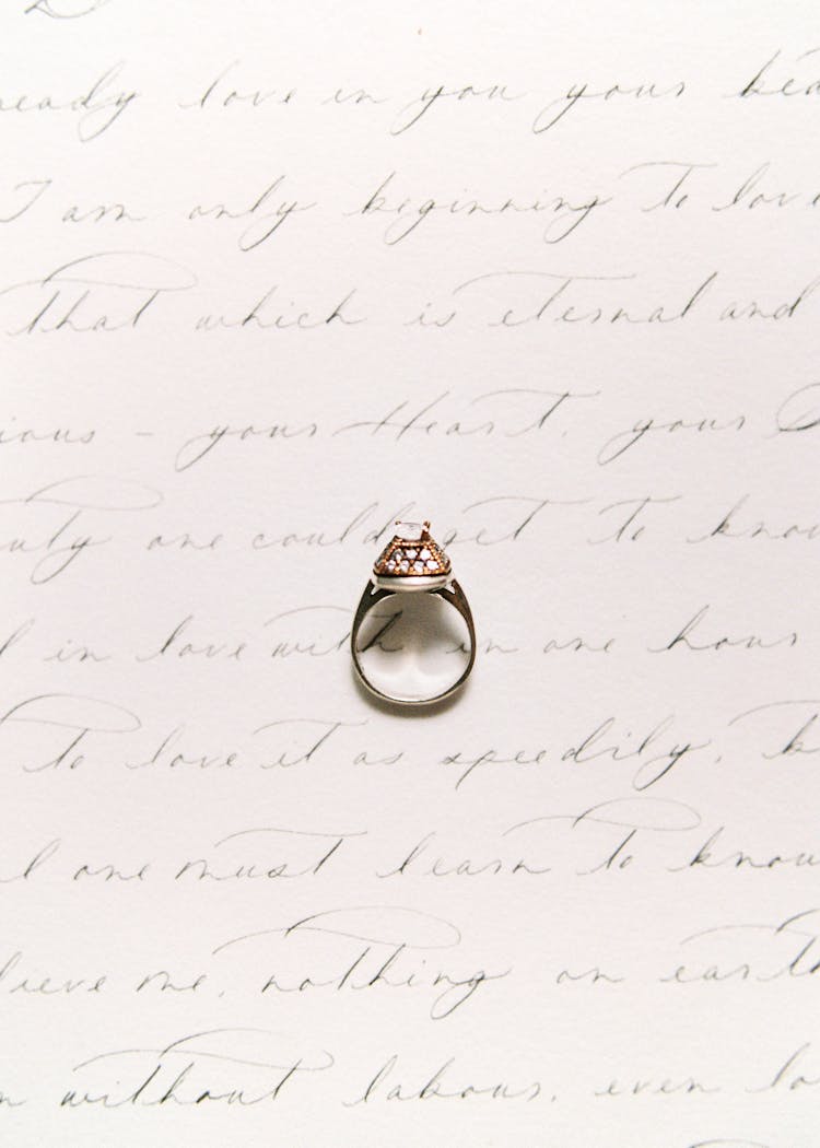 Diamond Ring On Top Of White Sheet Of Paper With Handwriting 