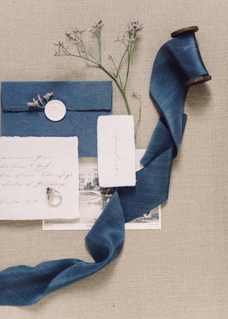 An Envelope With Letter And Ring Beside Blue Ribbon