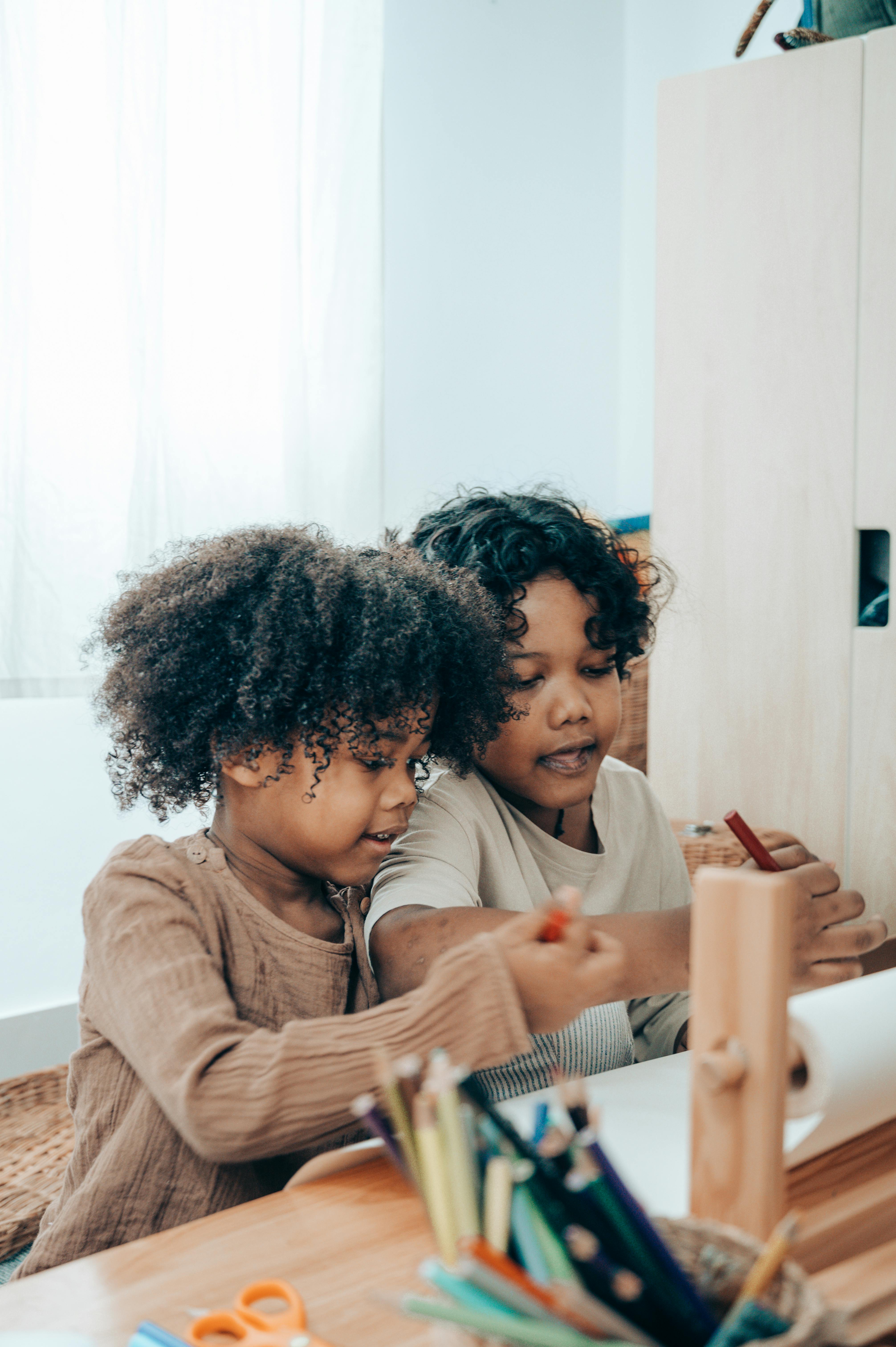 content black siblings drawing with felt pens at desk