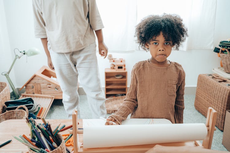 Shy African American Girl With Pencil Sitting Near Crop Sibling