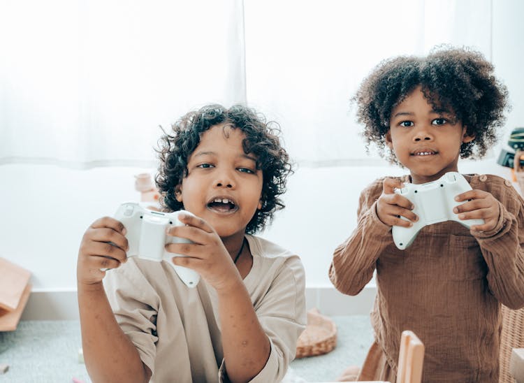 Cheerful Black Children Playing With Game Pads In Room