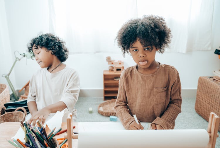 African American Girl With Tongue Out Drawing On Paper Near Sibling