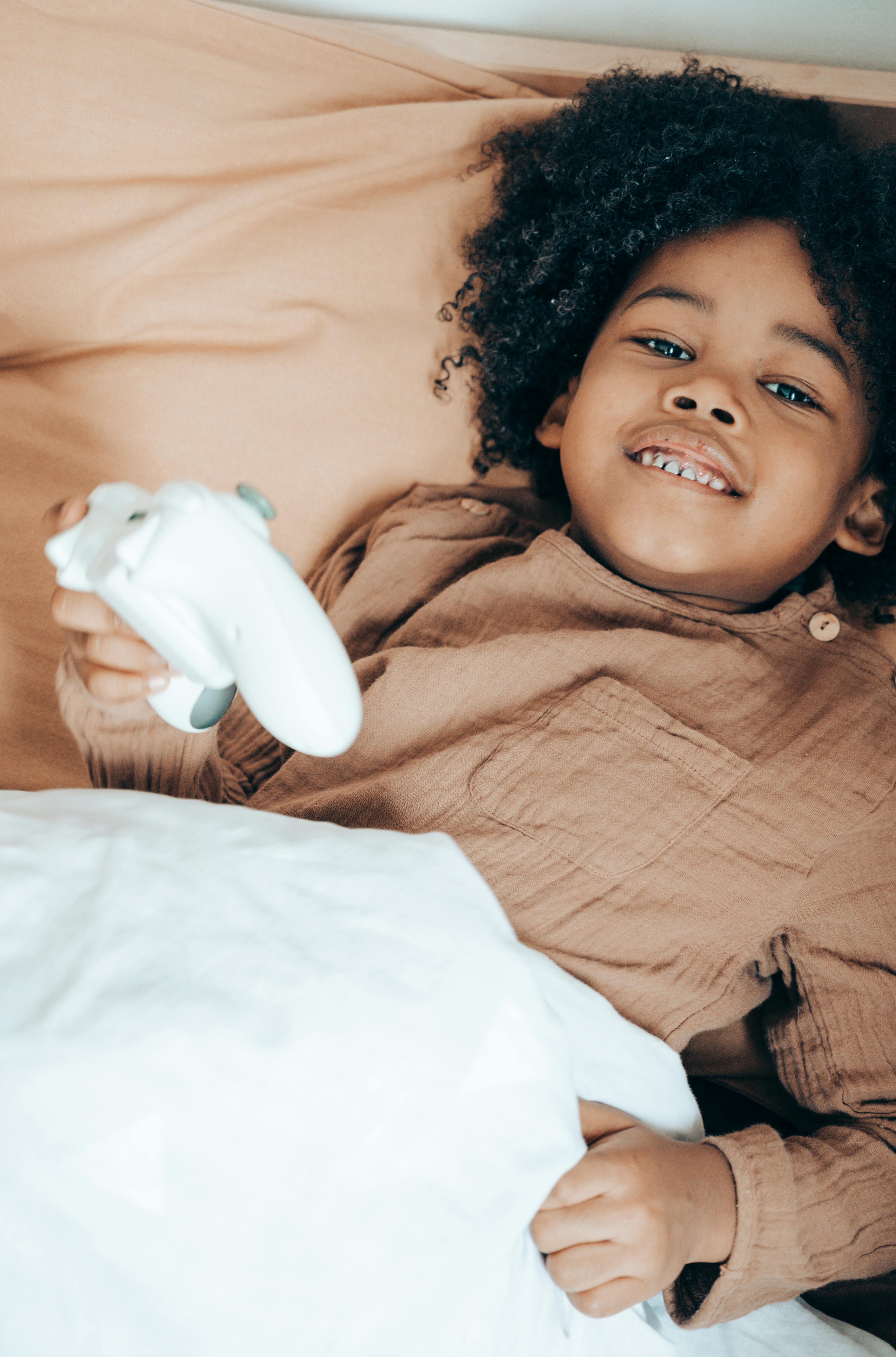 cheerful black girl playing with joystick in bed in morning