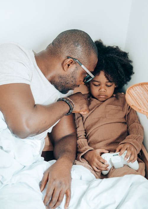 Loving black father spending free time with cute daughter in bed at home