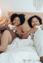 From above of happy African American sisters in domestic wear lying on comfortable bed together and playing video game with gamepads during free time at home