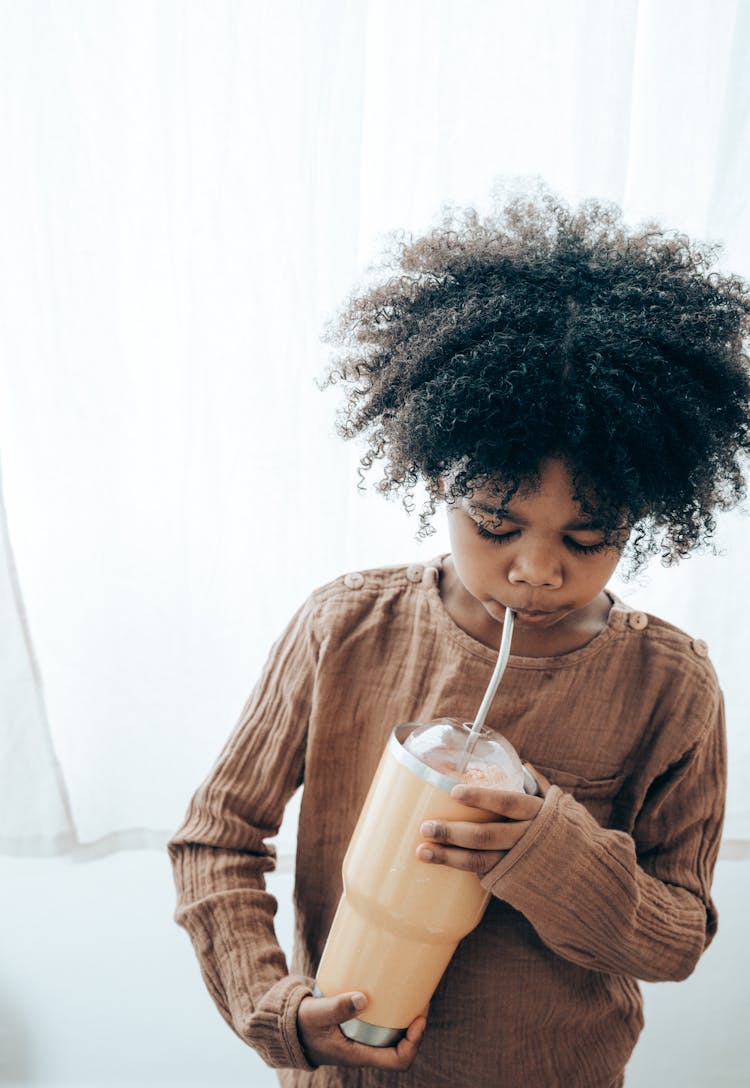 Ethnic Kid Drinking Fresh Beverage In Cafe