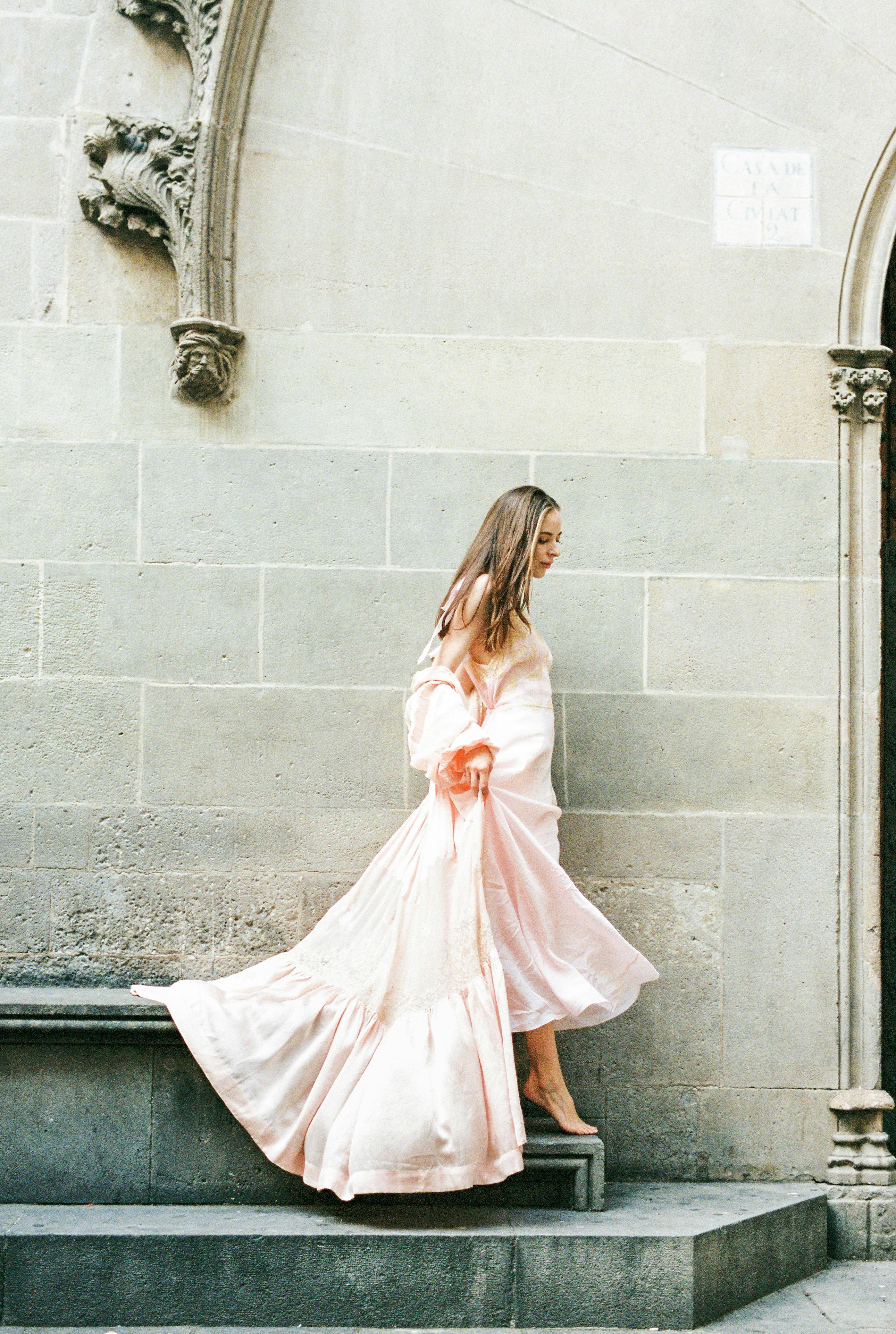 woman in pink long sleeve dress standing beside gray concrete wall