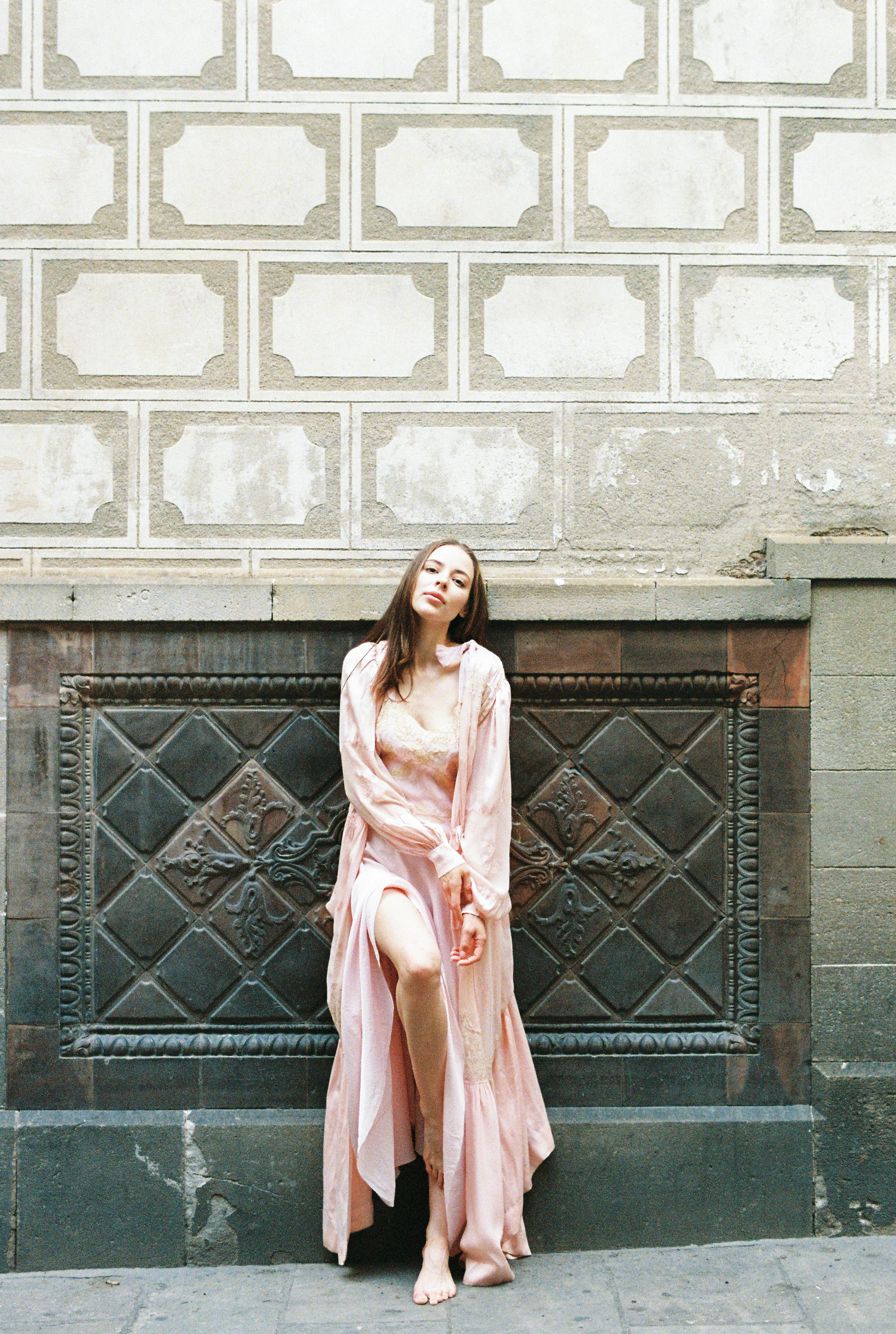 woman in pink dress standing leaning on a wall