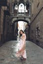一位身着粉红连衣裙的女子，优雅地回眸，走过一条历史悠久的巷子