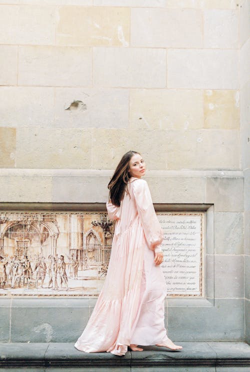 無料 白いコンクリートの壁の近くに立っているピンクの長袖のドレスの女性 写真素材