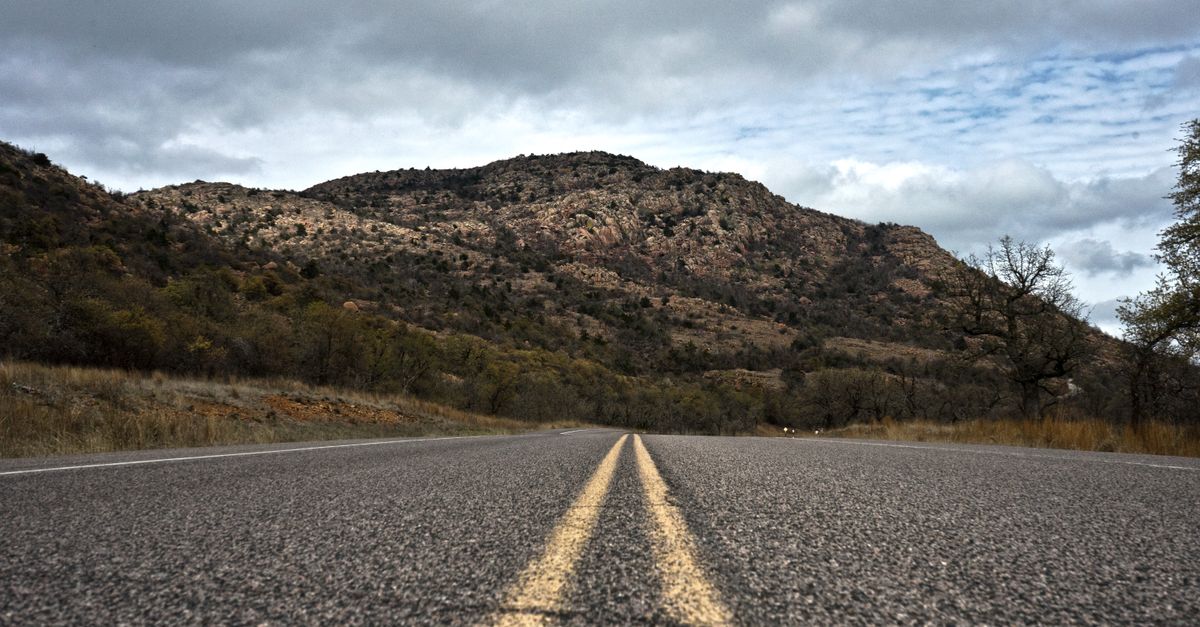 Empty road leading to the scenic Oklahoma mountains under a cloudy sky.