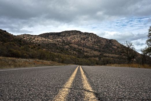 Empty road leading to the scenic Oklahoma mountains under a cloudy sky.
