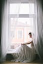 优雅的新娘穿着飘逸的礼服，坐在挂着透明窗帘的窗前，散发着优雅的气质