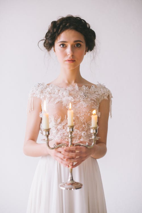 Woman in White Dress Holding White and Gold Colored Candle Holder
