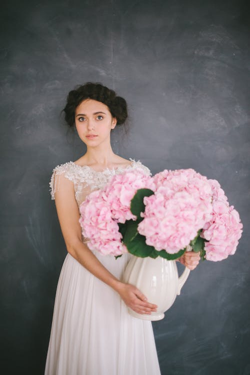 一個年輕的女人拿著一個花瓶，上面有粉紅色的花朵