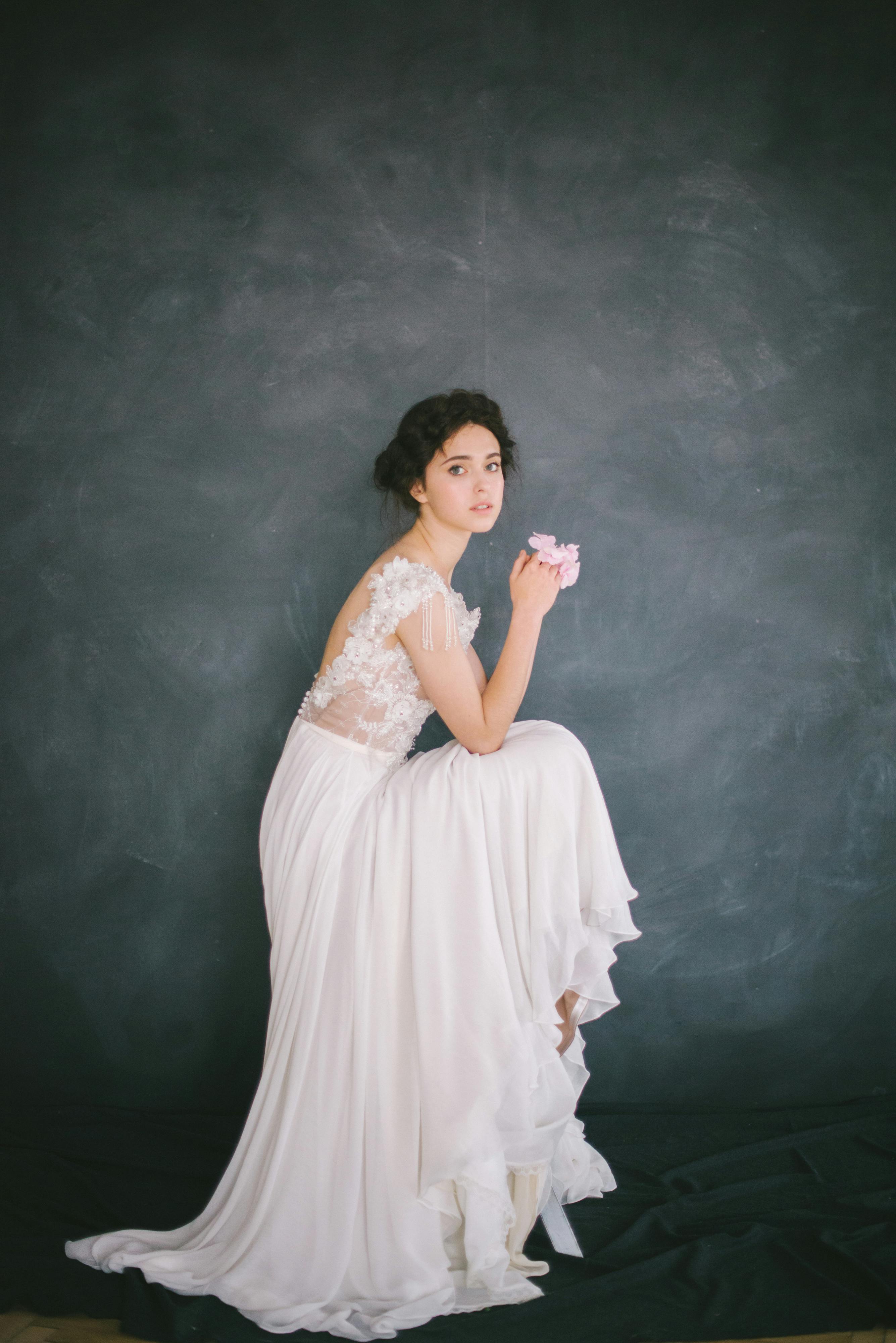 在黑暗的工作室背景下，优雅的新娘身着蕾丝礼服，手持淡粉色花朵摆着姿势