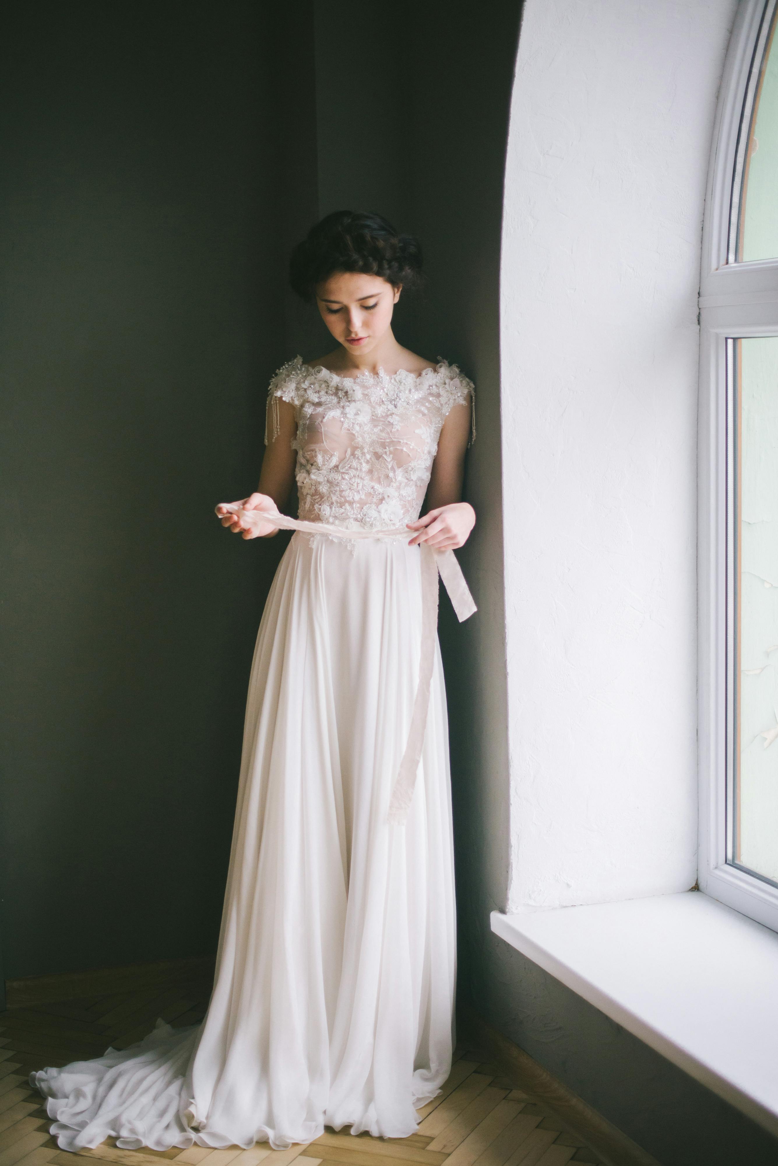 一位穿着优雅蕾丝婚纱的新娘在窗前优雅地摆着姿势