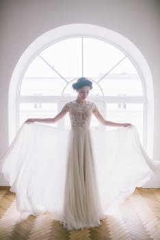 A graceful bride posing in a luxurious gown near a backlit arched window, embodying elegance and charm.
