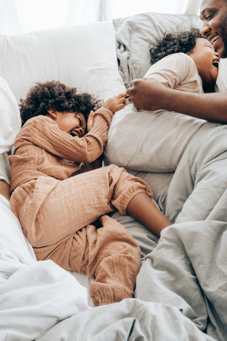 Happy Ethnic Kids And Man Playing On Bed In Morning