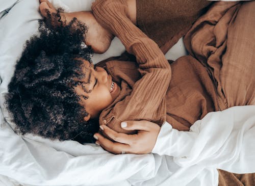 Happy black kid playing in bed at home