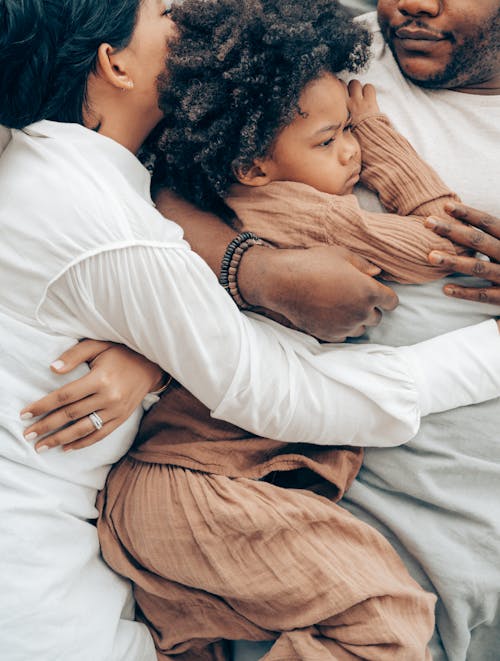 Free Top view of charming African American child and parents in pajamas lying together hugging each other on bed Stock Photo