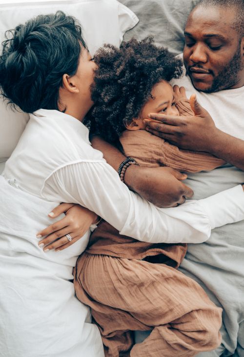 Free From above of black  child in pajama lying in bed with parents cuddled son together and touching face with care Stock Photo