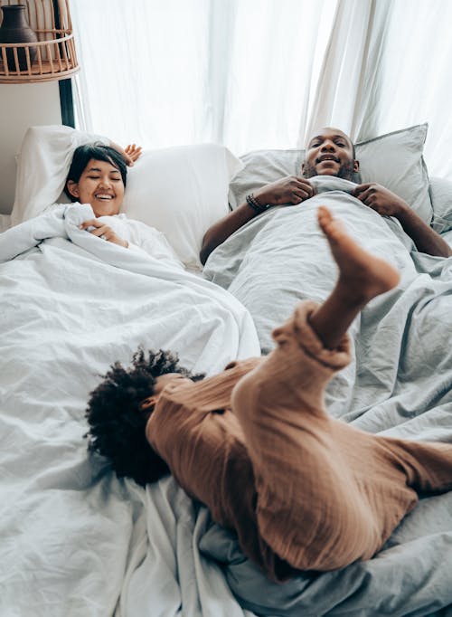 Free African American kid fooling around parents lying in bed Stock Photo