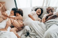 From above of father and elderly child laughing in bed near mother and younger kid patting dog while resting in weekend together