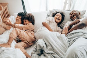From above of father and elderly child laughing in bed near mother and younger kid patting dog while resting in weekend together
