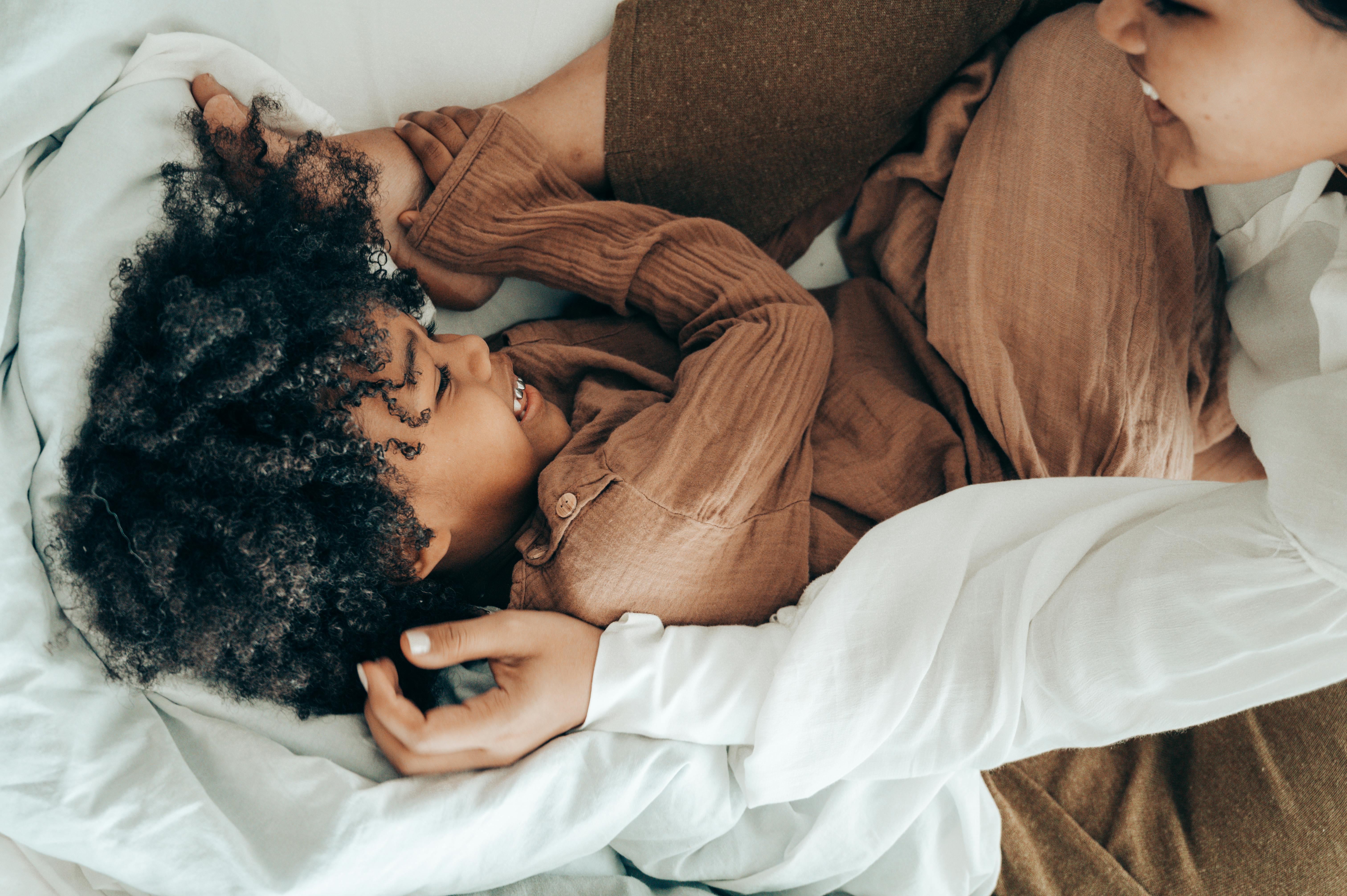 happy ethnic kid playing with mom on bed