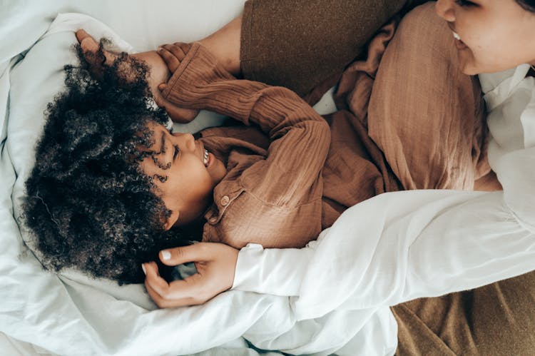 Happy Ethnic Kid Playing With Mom On Bed